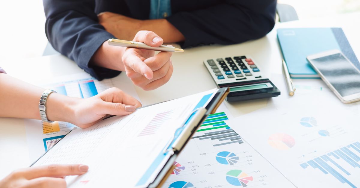 two people looking at paperwork on a desk with a calculator